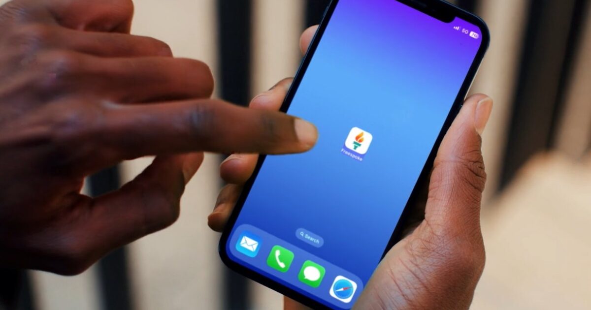 Hand holding a smartphone with a blue gradient background, featuring the FreeSpoke app icon on the screen.