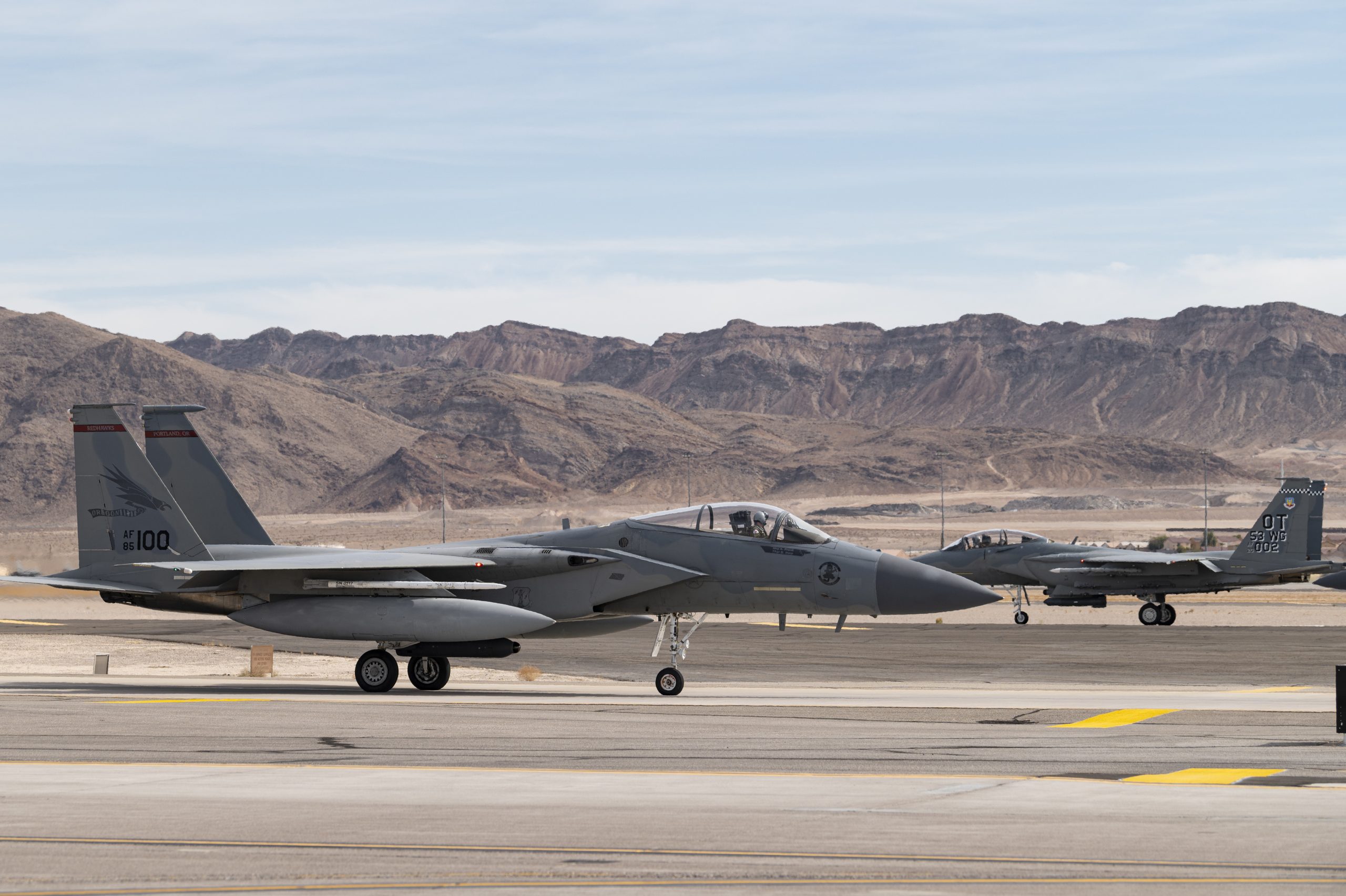 An F-15EX Eagle II Fighter Jet assigned to the 85th Test and Evaluation Squadron, Eglin Air Force Base, Florida, takes off and an F-15C Eagle assigned to the 123rd Fighter Squadron, Portland Air National Guard Base, Oregon, taxis to the runway at Nellis Air Force Base, Nevada, Oct. 20, 2021. Aircraft from Nellis AFB, Eglin AFB Florida, and the Oregon Air National Guard are providing support for the Test and Evaluation of the F-15EX in operationally realistic scenarios to determine how effective and suitable the aircraft is at accomplishing its air-to-air mission for future Air Force use. (U.S. Air Force photo by William R. Lewis)