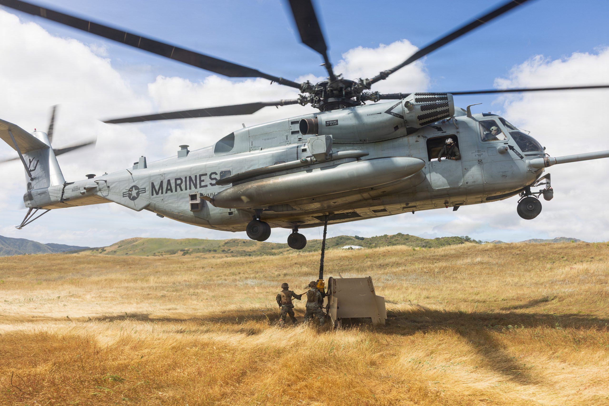 U.S. Marine Corps Cpl. Naquis Williams (left), alongside Pfc. Matthew Reich, and Cpl. Luke Greene, all logistics specialist with 1st Distribution Support Battalion, Combat Logistics Regiment 1, 1st Marine Logistics Group, attach a steel target to a CH-53E Super Stallion helicopter assigned to Heavy Helicopter Squadron 465 (HMH-465), 3rd Marine Aircraft Group 16, 3rd Marine Aircraft Wing, during helicopter support team training on Marine Corps Base Camp Pendleton, California, April 21, 2026. While executing HST training, Marines with 1st DSB improved proficiency securing cargo while coordinating with aircrew, conditioning themselves to safely prepare external lifts in austere environments. (U.S. Marine Corps photo by Sgt. Mary Torres)