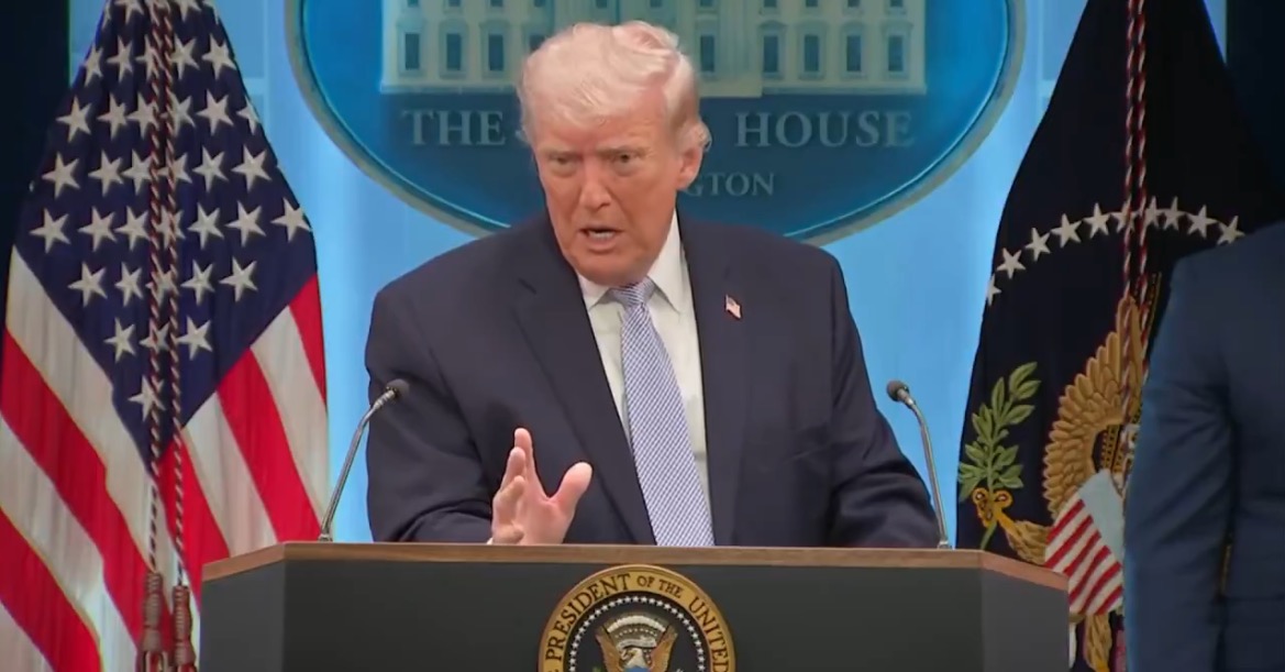 Donald Trump speaks at a press conference in the White House briefing room, flanked by American flags and the presidential seal.