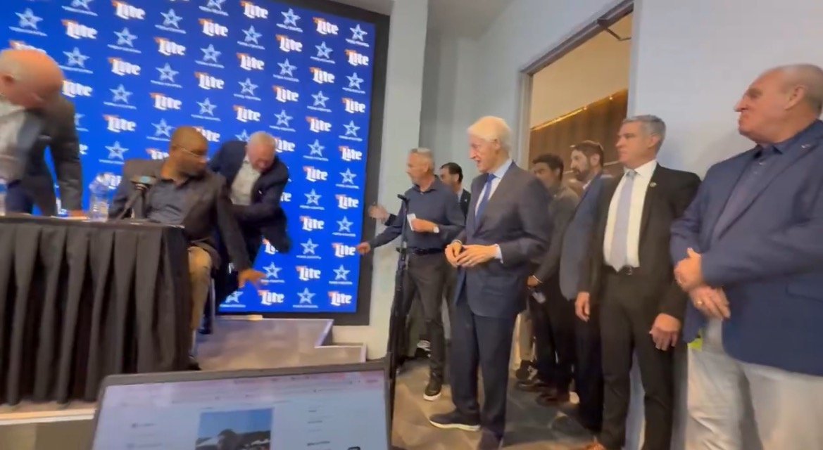 Press conference featuring multiple individuals at a podium with a branded backdrop, capturing a moment of interaction and engagement among attendees.