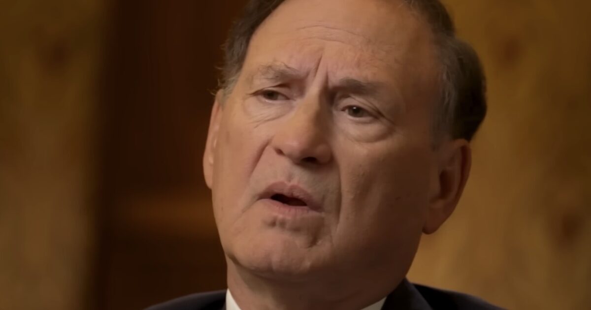 Man in a suit speaking thoughtfully, with a blurred background, conveying a serious discussion or interview setting.