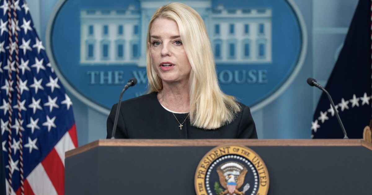 Press briefing at the White House featuring a female speaker in a black outfit, with the presidential seal and American flags in the background.