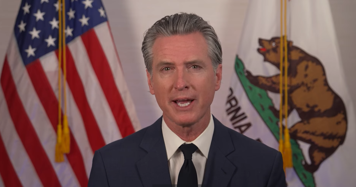 California Governor speaking in front of the American and California flags, addressing key state issues in a formal setting.
