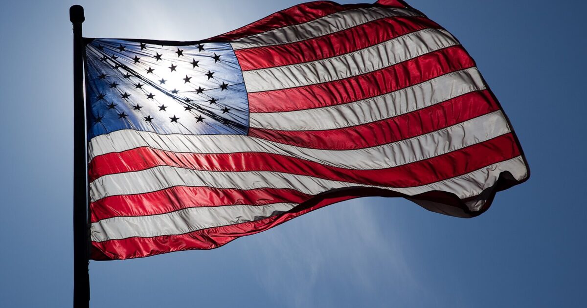 American flag waving against a clear blue sky, showcasing its vibrant red, white, and blue colors and stars.