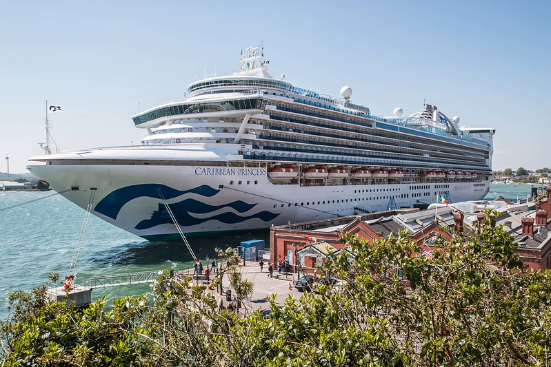 Caribbean Princess cruise ship docked near a waterfront with people and buildings visible in the foreground.