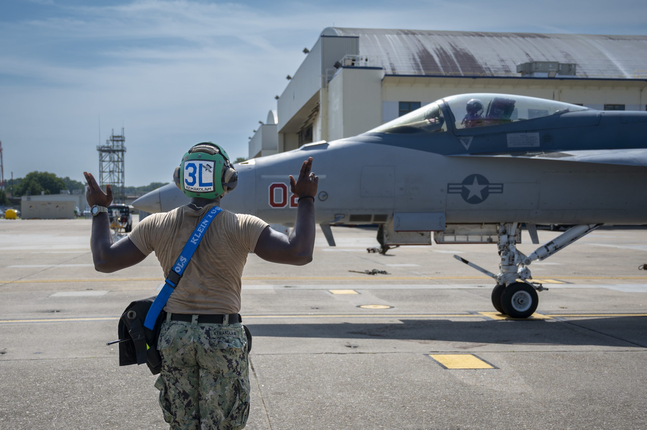 230830-N-IC246-1036 Naval Air Station Oceana, Va. (August 30, 2023) – Petty Officer 3rd Class Clinton Kemakolam, currently assigned to Fighter Squadron Composite Twelve (VFC-12), signals to the pilot of an F/A-18F Super Hornet on a flightline on Naval Air Station Oceana. VFC-12 provides strategic depth and operational support to the U.S. Navy by training and qualifying F/A-18 A-D aviators while maintaining warfighting readiness. (U.S. Navy photo by Mass Communication Specialist 1st Class Raymond Maddocks)