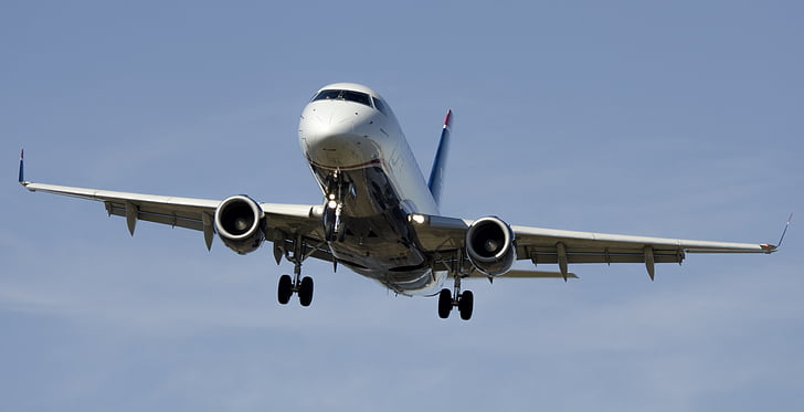 Commercial airplane approaching for landing against a clear blue sky, showcasing its wings and landing gear.