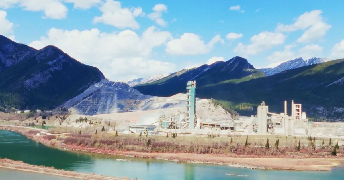 Industrial facility near a river with mountains in the background, showcasing a blend of nature and manufacturing infrastructure.
