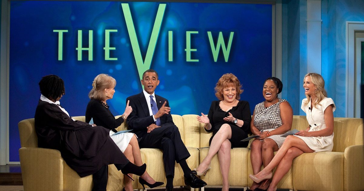 Barack Obama appears on The View, engaging with the hosts in a lively discussion while seated on a yellow couch.