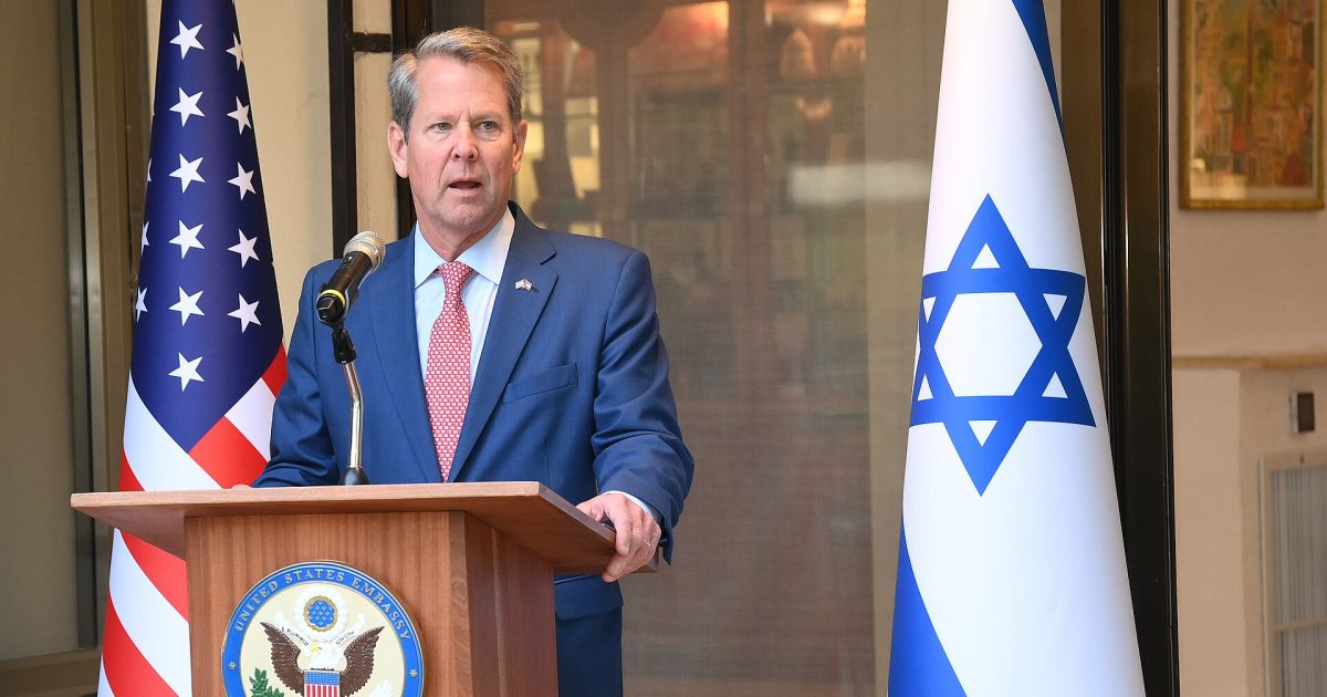 Official speaking event featuring a representative at the United States Embassy in Jerusalem, with American and Israeli flags in the background.