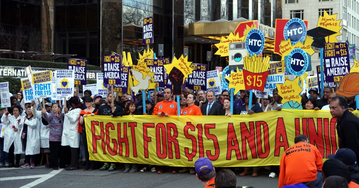 Workers rally for a $15 minimum wage and union rights, holding colorful signs in an urban setting, advocating for economic justice and fair treatment.