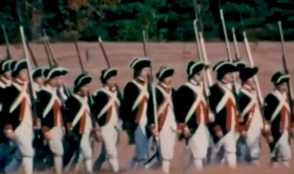 Historical reenactors in traditional Revolutionary War uniforms march in formation, showcasing military traditions and attire from the 18th century.