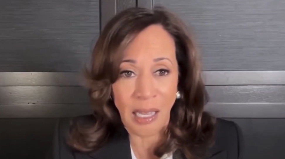 Close-up of a woman with medium-length brown hair speaking passionately in front of a dark background, conveying a serious message.