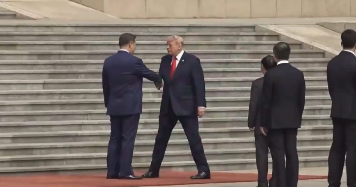 World leaders Xi Jinping and Donald Trump shake hands on steps during a formal meeting, surrounded by security personnel.