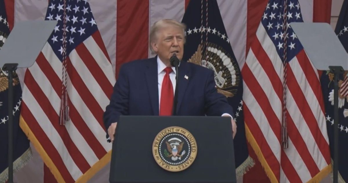 Donald Trump delivering a speech at a podium adorned with the presidential seal, flanked by American flags.