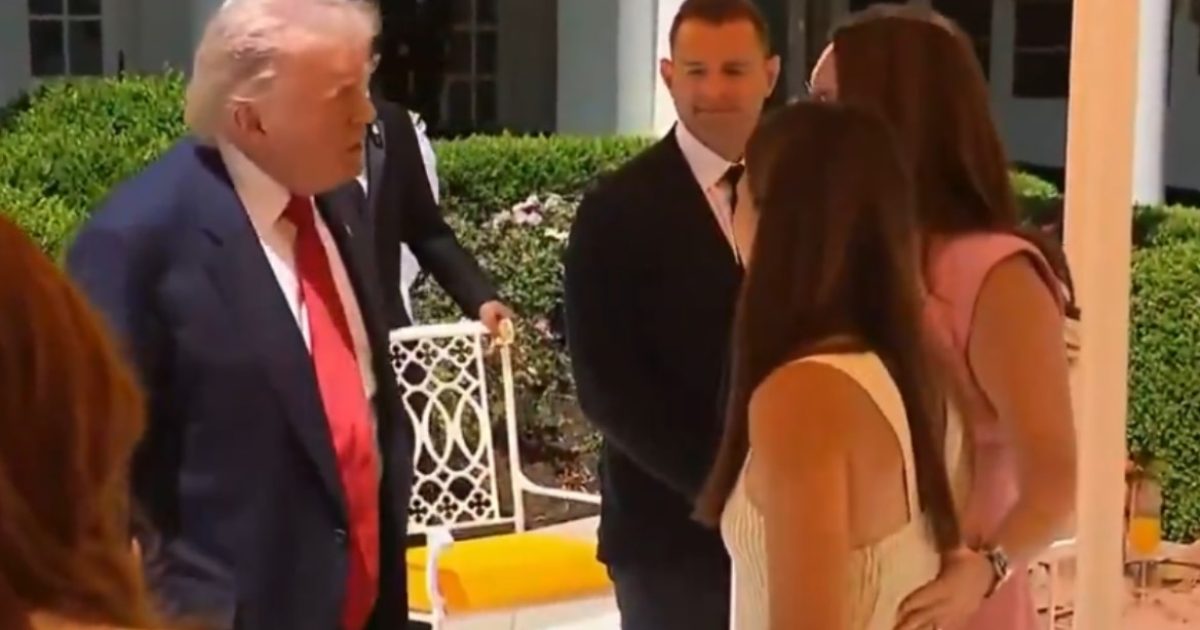 Donald Trump engages in conversation with several individuals at a social gathering in an outdoor setting.