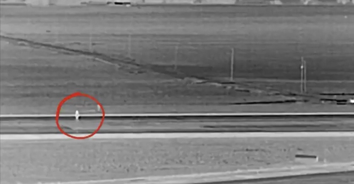 Thermal image showing a figure in a vast open field, highlighted for visibility against the landscape.
