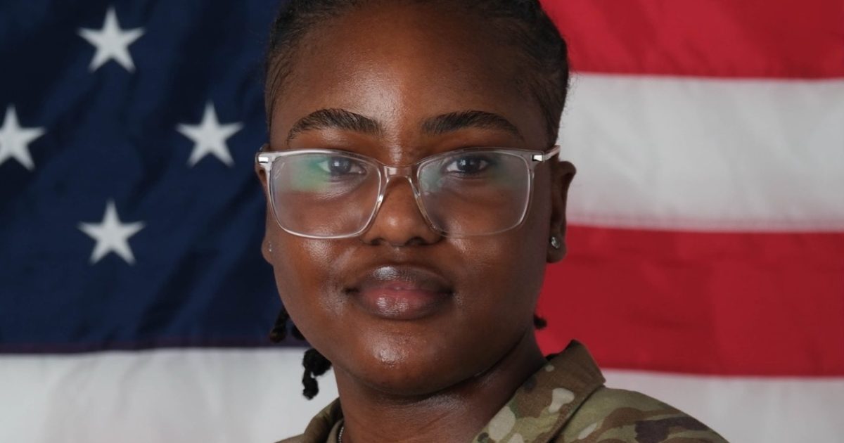 Portrait of a military service member in uniform, smiling confidently against a backdrop of the American flag.