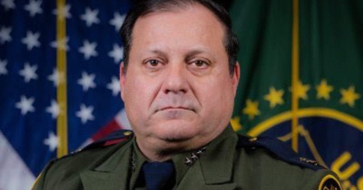 Portrait of a law enforcement officer in uniform, standing in front of the American flag and a departmental emblem, conveying authority and professionalism.