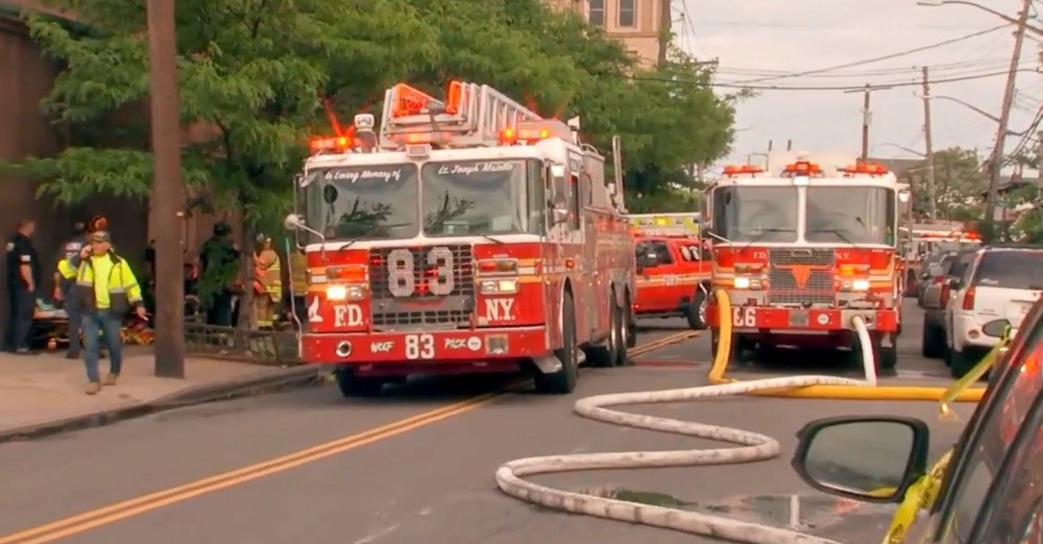 Fire trucks responding to an emergency scene with firefighters and equipment on a city street, showcasing fire safety and emergency response efforts.