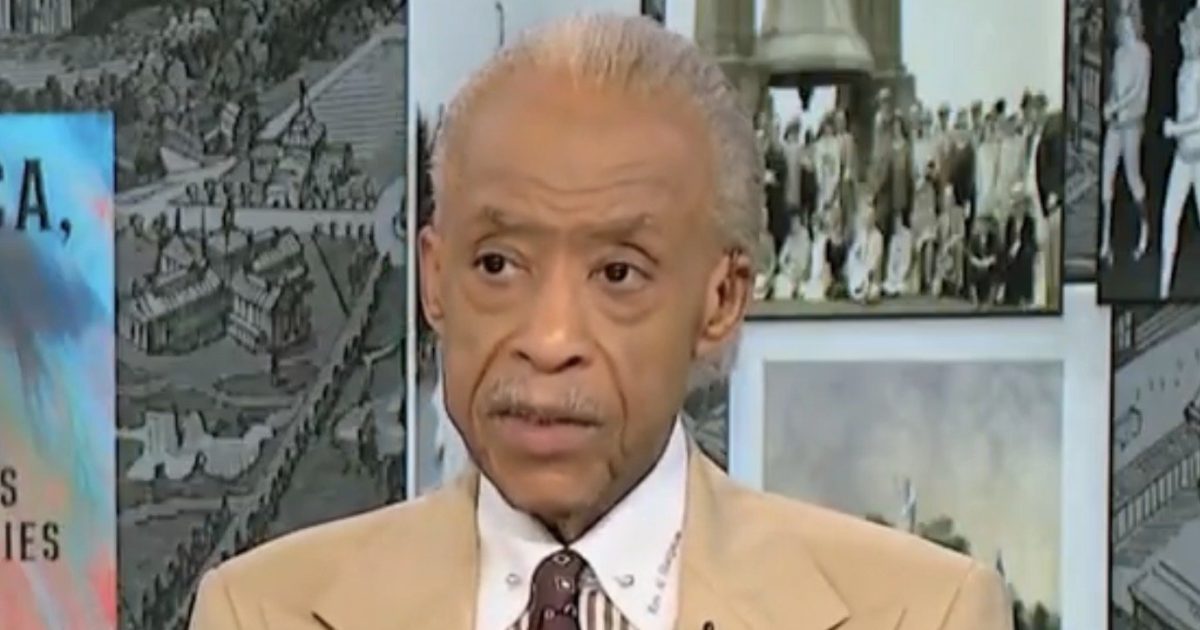 Al Sharpton speaks during a televised interview, wearing a beige suit and patterned tie, with historical images in the background.
