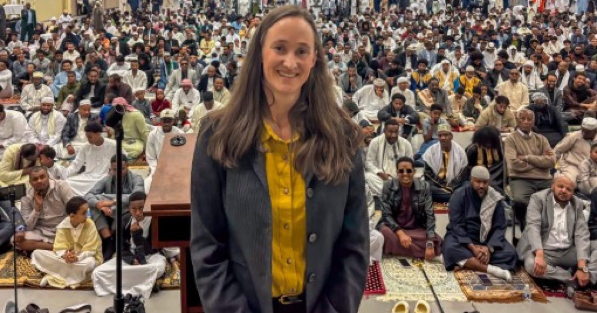 Woman smiling in front of a large crowd gathered for a religious event, showcasing cultural diversity and community engagement.