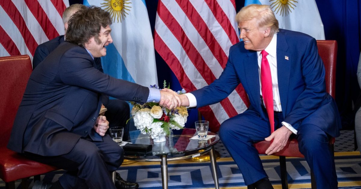 Donald Trump shakes hands with an official in front of U.S. and Argentine flags during a diplomatic meeting.