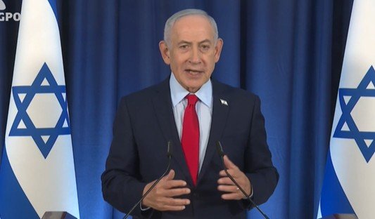 Israeli Prime Minister Benjamin Netanyahu delivers a speech with Israeli flags in the background.
