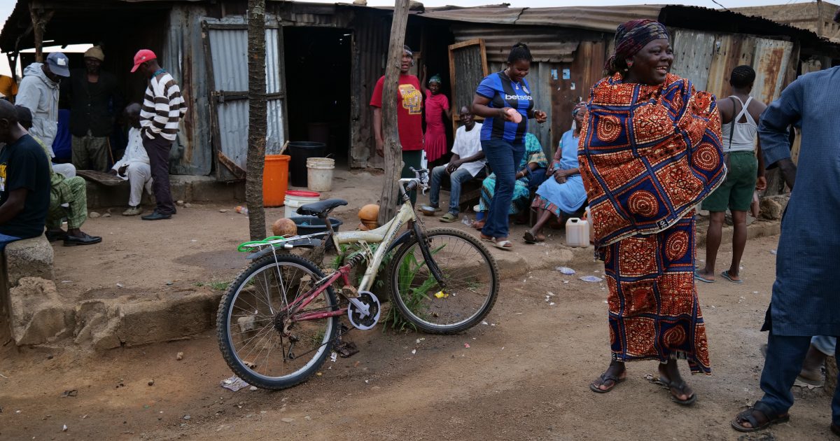 A lively street scene in a local community with people engaging in conversation, a woman in traditional attire, and a bicycle parked nearby.