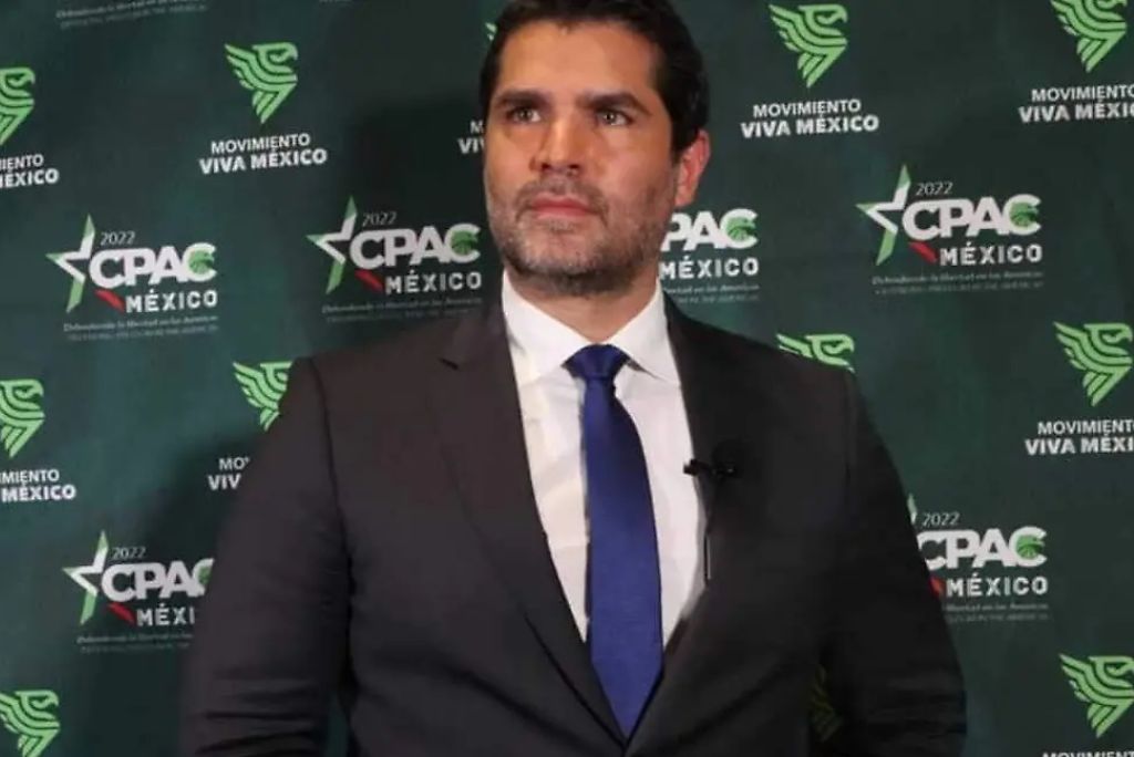 Man in formal attire standing in front of a CPAC Mexico backdrop, promoting the Movimiento Viva Mexico event.