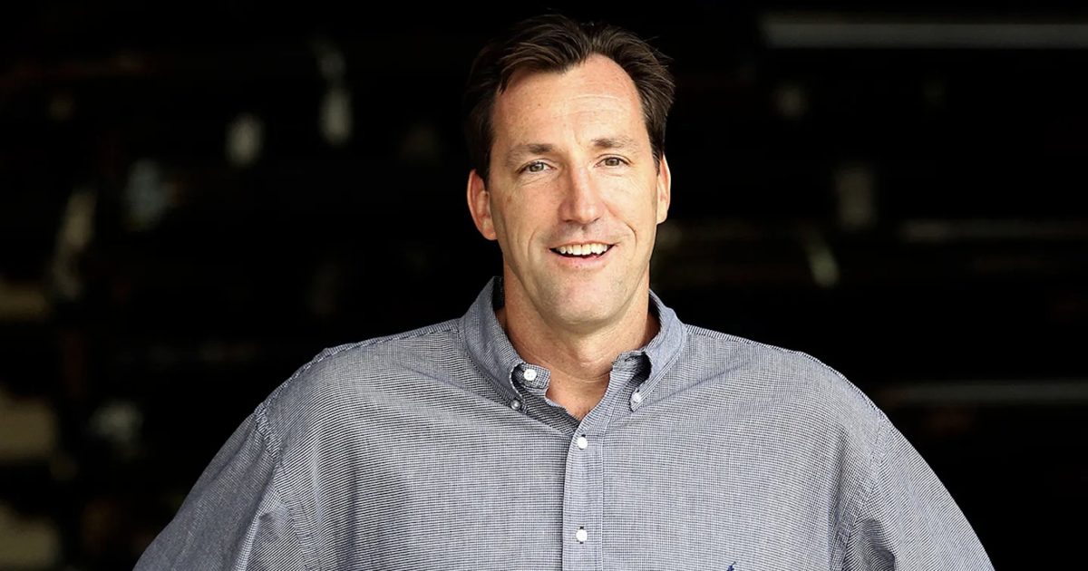Smiling man in a button-up shirt stands in front of a dark background, exuding confidence and approachability.