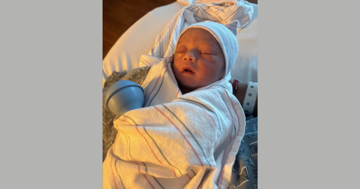 Newborn baby swaddled in a hospital blanket, peacefully sleeping with a blue bottle beside them, showcasing a serene moment in a maternity ward.