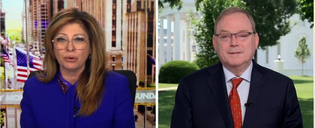 News segment featuring a female host in a blue outfit and a male guest in a suit, discussing current events outdoors at the White House.