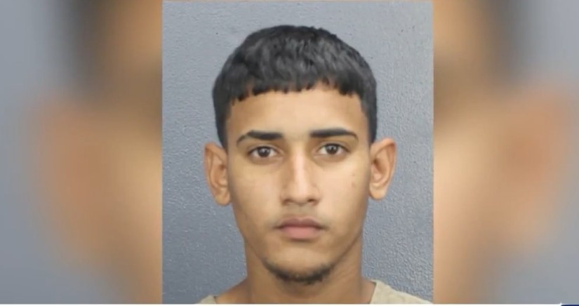 Mugshot of a young male with short hair, wearing a beige inmate uniform, against a gray background.