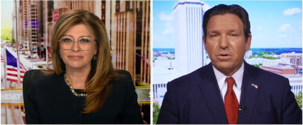 News segment featuring a female host and male politician discussing current events, with a cityscape backdrop and American flags visible.