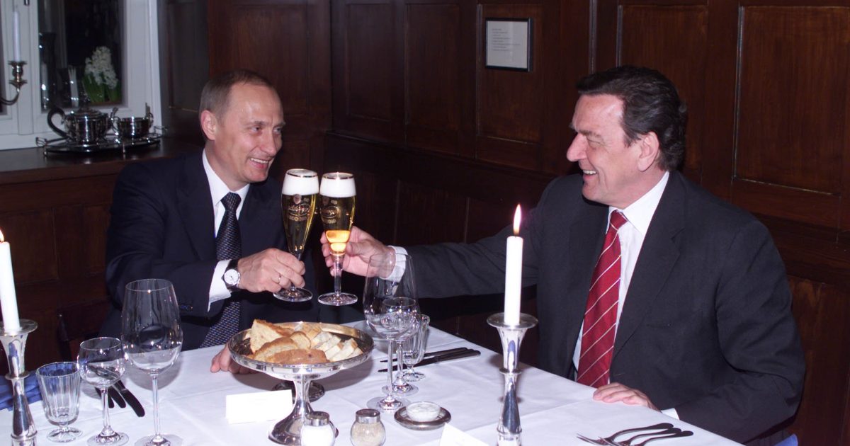 Two men clink glasses of beer during a formal dinner, surrounded by an elegant table setting with candles and fine dining utensils.