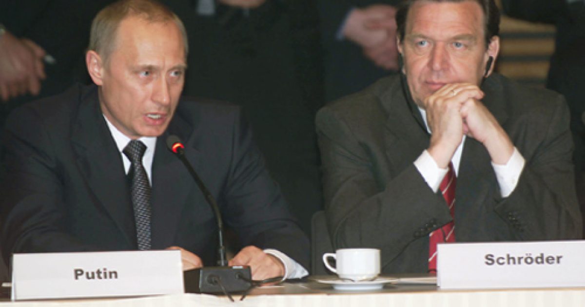 Vladimir Putin and Gerhard Schröder participate in a formal discussion at a conference table, highlighting diplomatic relations between Russia and Germany.
