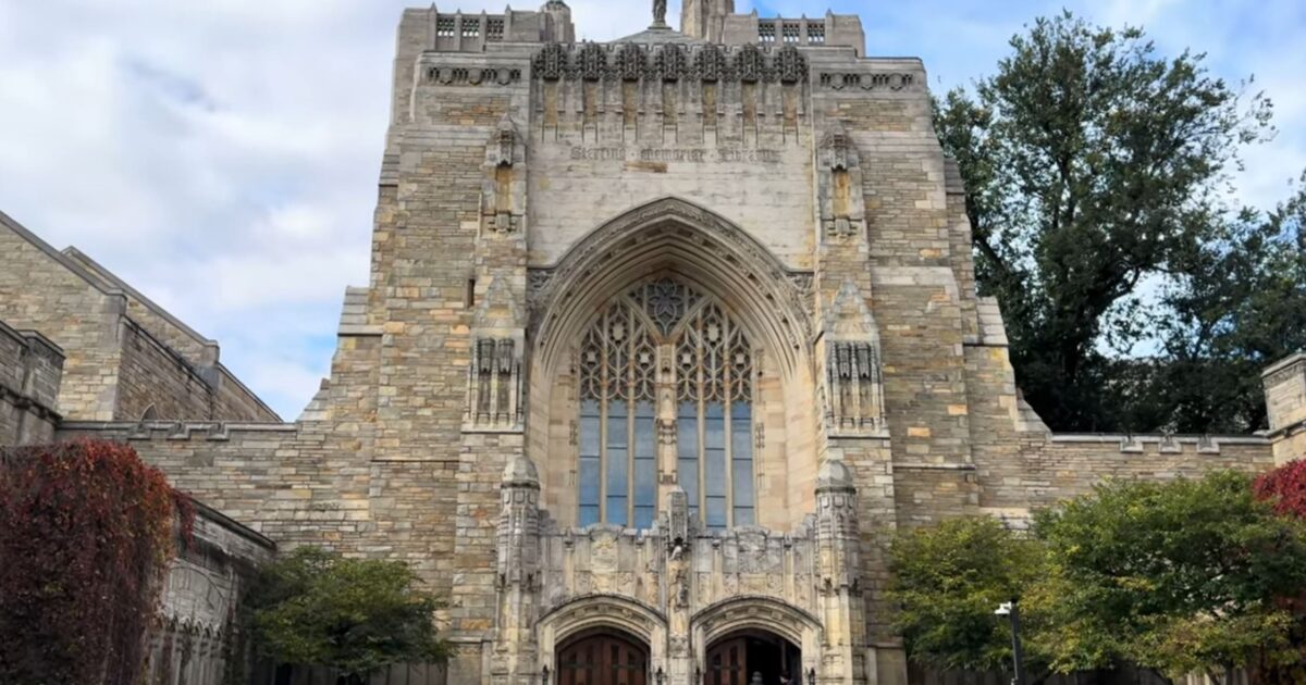 Gothic-style architecture of Sterling Memorial Library at Yale University, featuring intricate stonework and large arched windows, surrounded by trees and greenery.