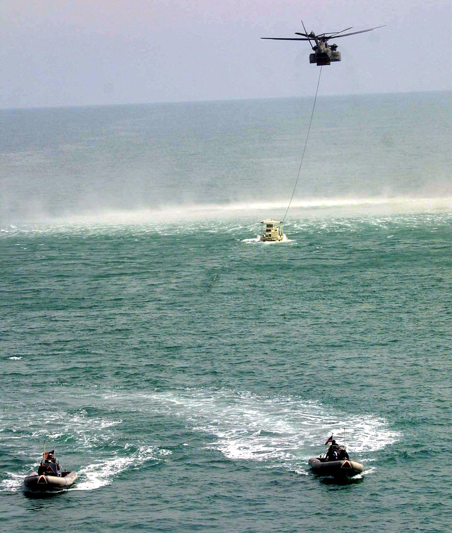 A US MH-53E military helicopter drags a MK 106 Combination escorted by two military Zodiak boats during an opperation off the USS Ponce to clear mines from Khor Abdullah at the entrance to Umm Qasr port in the western Gulf 29 March 2003. Sharp differences have emerged between the United States and Britain on who should rebuild Iraqi port Umm Qasr after the war, as non-US firms have been almost completely excluded from the tenders process. Umm Qasr is Iraq's only deep-water seaport on its short Gulf coastline, which lies on the western side of the Fao Peninsula 460 kilometers (280 miles) south of Baghdad. AFP PHOTO/Rabih MOGHRABI (Photo by RABIH MOGHRABI / AFP) (Photo by RABIH MOGHRABI/AFP via Getty Images)