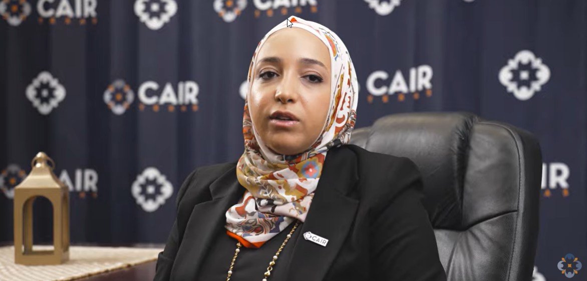 Woman in a hijab seated in front of a CAIR backdrop, discussing community issues and advocacy.
