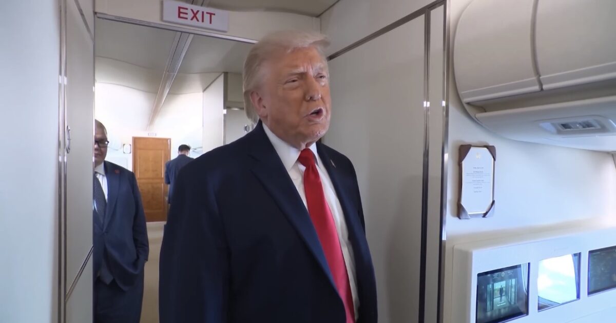 Donald Trump speaking inside a private jet with an exit sign in the background, showcasing a luxurious travel environment.