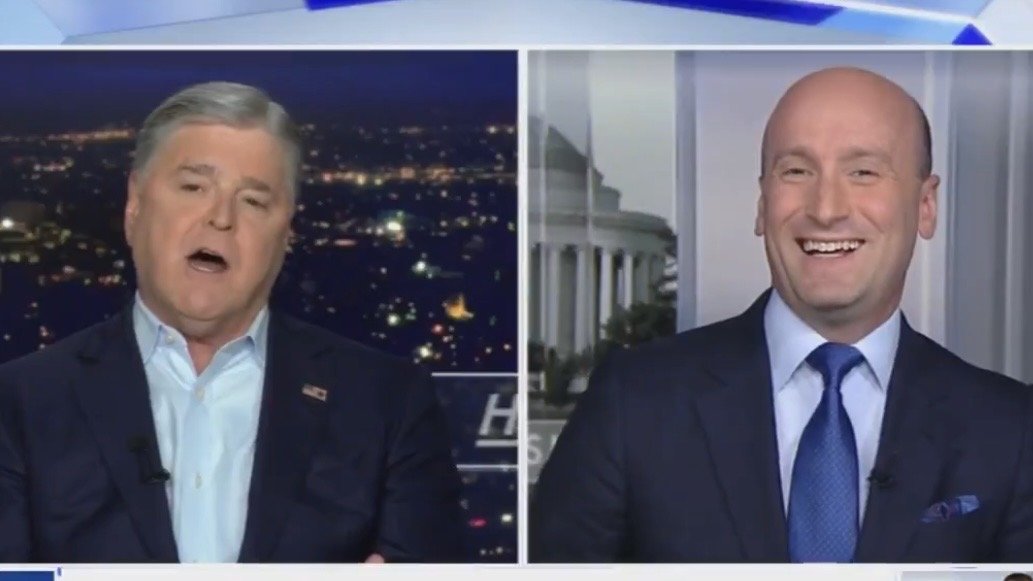 Two men engaged in a lively discussion on a television news program, with a city skyline visible in the background.
