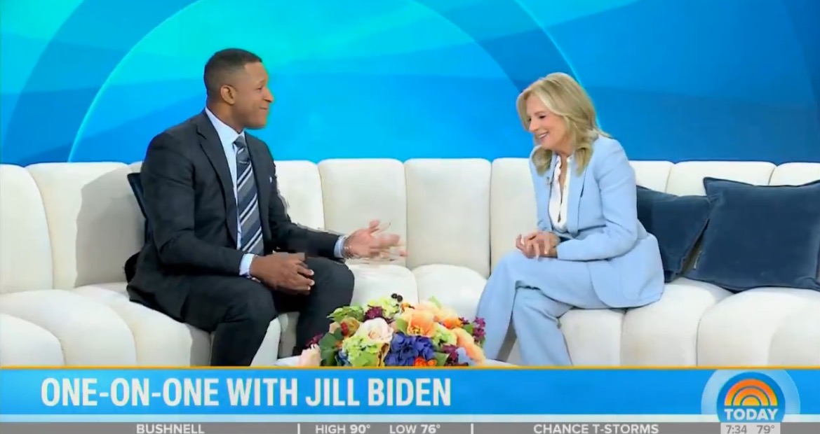 Jill Biden discusses various topics during a one-on-one interview on a talk show set, featuring a floral arrangement in the foreground.