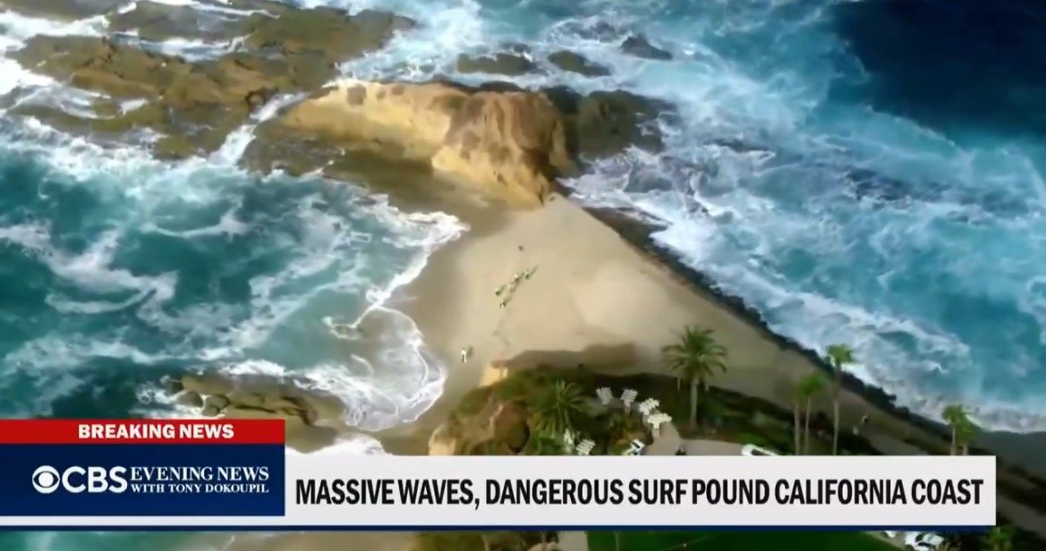 Aerial view of massive waves crashing against the rocky coastline of California, highlighting the dangerous surf conditions along the beach.