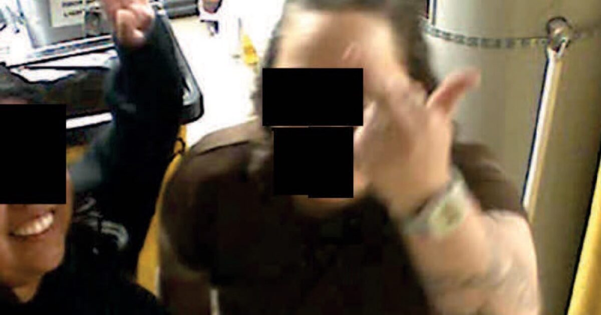 Two individuals posing playfully in a kitchen, one making a hand gesture while the other smiles, with blurred faces for privacy.