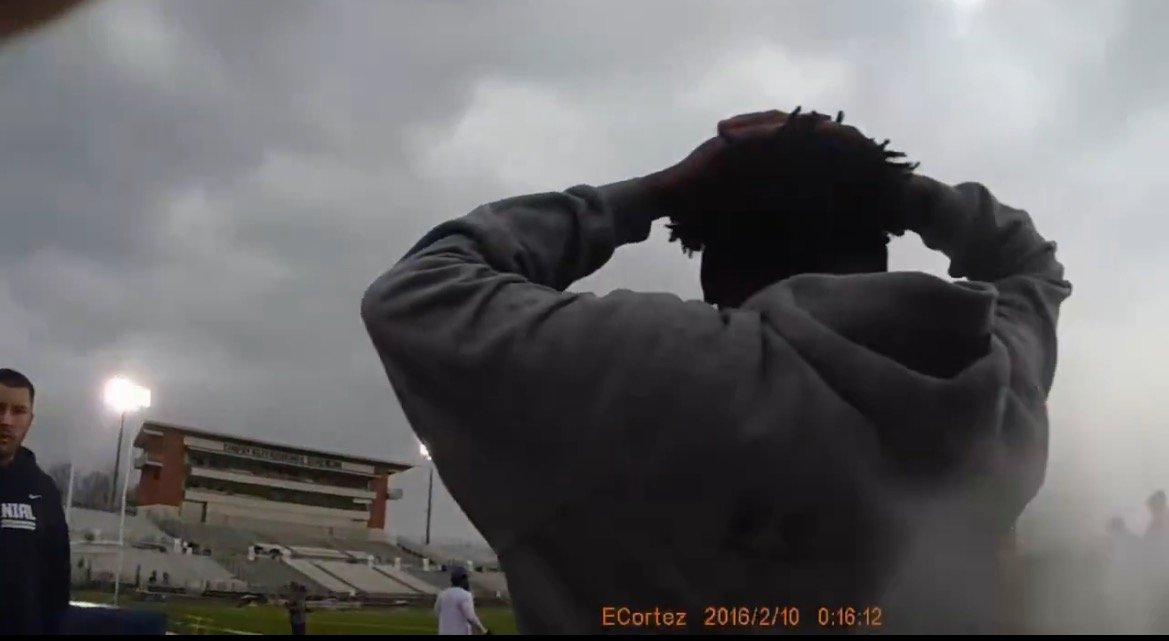 A person stands with hands on their head, looking towards a stadium under cloudy skies, with another individual visible nearby.