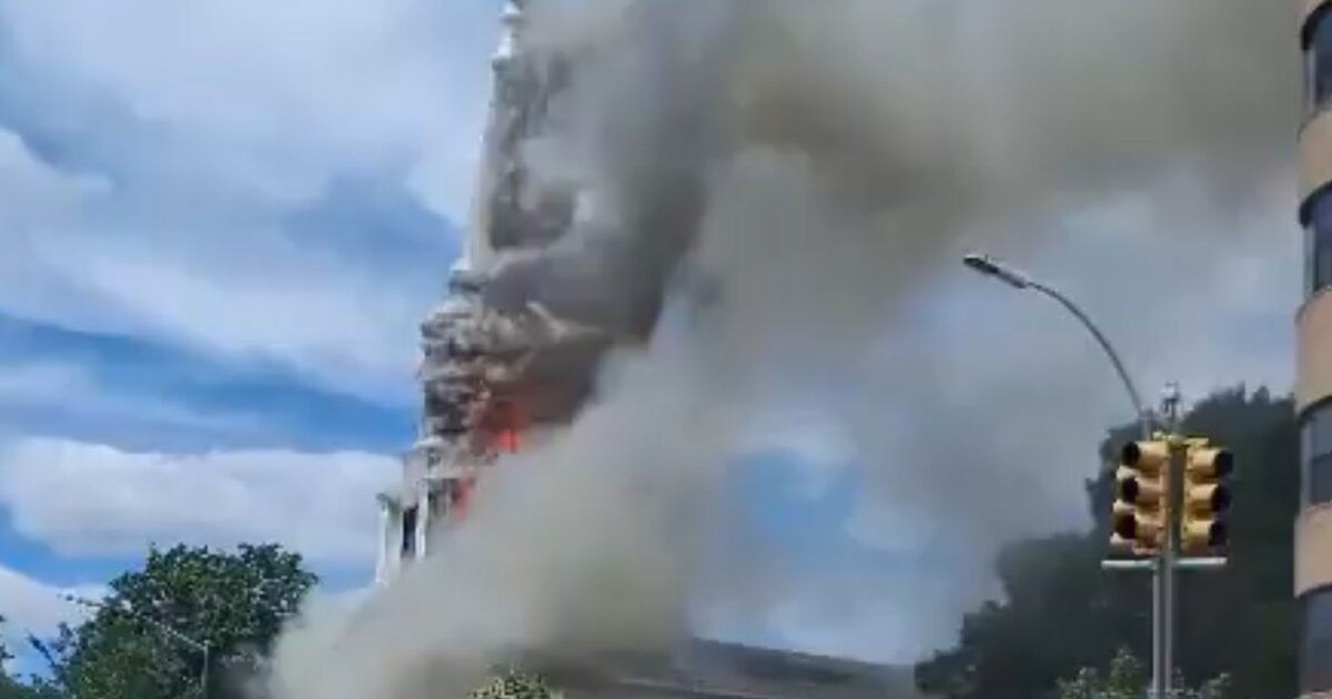 Smoke billowing from a building during a fire, with a clear blue sky and traffic lights in the foreground.