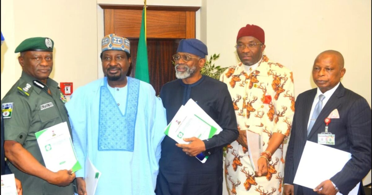 Group of Nigerian officials in formal attire holding documents, including a police officer and government representatives, during a meeting in an office setting.