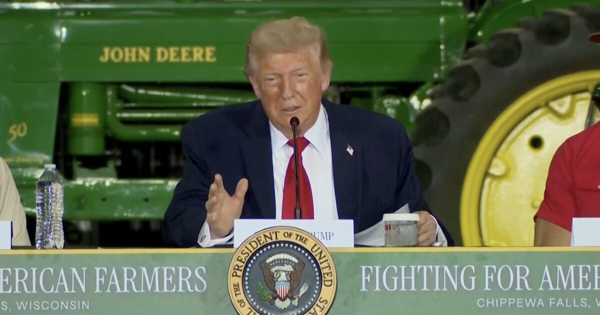 Donald Trump speaks at a press event for farmers in Chippewa Falls, Wisconsin, with a John Deere tractor visible in the background.